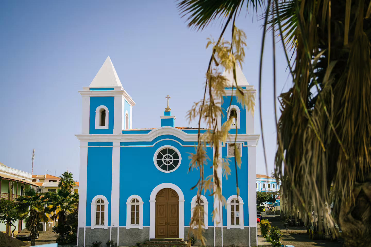 Vibrant blue church surrounded by palm trees under a clear sky on Fogo Island, highlighting cultural architecture.