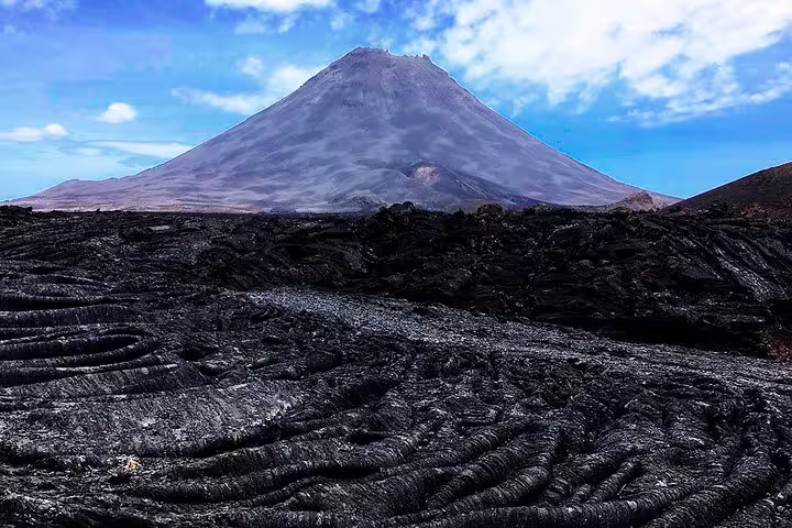 Majestic Fogo Island volcano with rugged black lava fields under a clear blue sky, inviting for trekking enthusiasts.