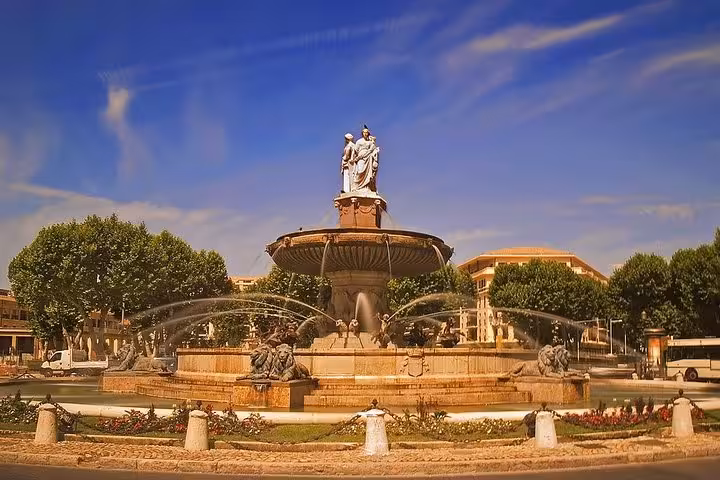 The iconic Fontaine de la Rotonde under a clear sky in Aix En Provence, surrounded by lush greenery and historic architecture.