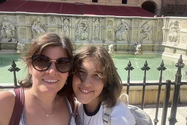 Two women smiling in front of the Fonte Gaia fountain in Siena's Piazza del Campo