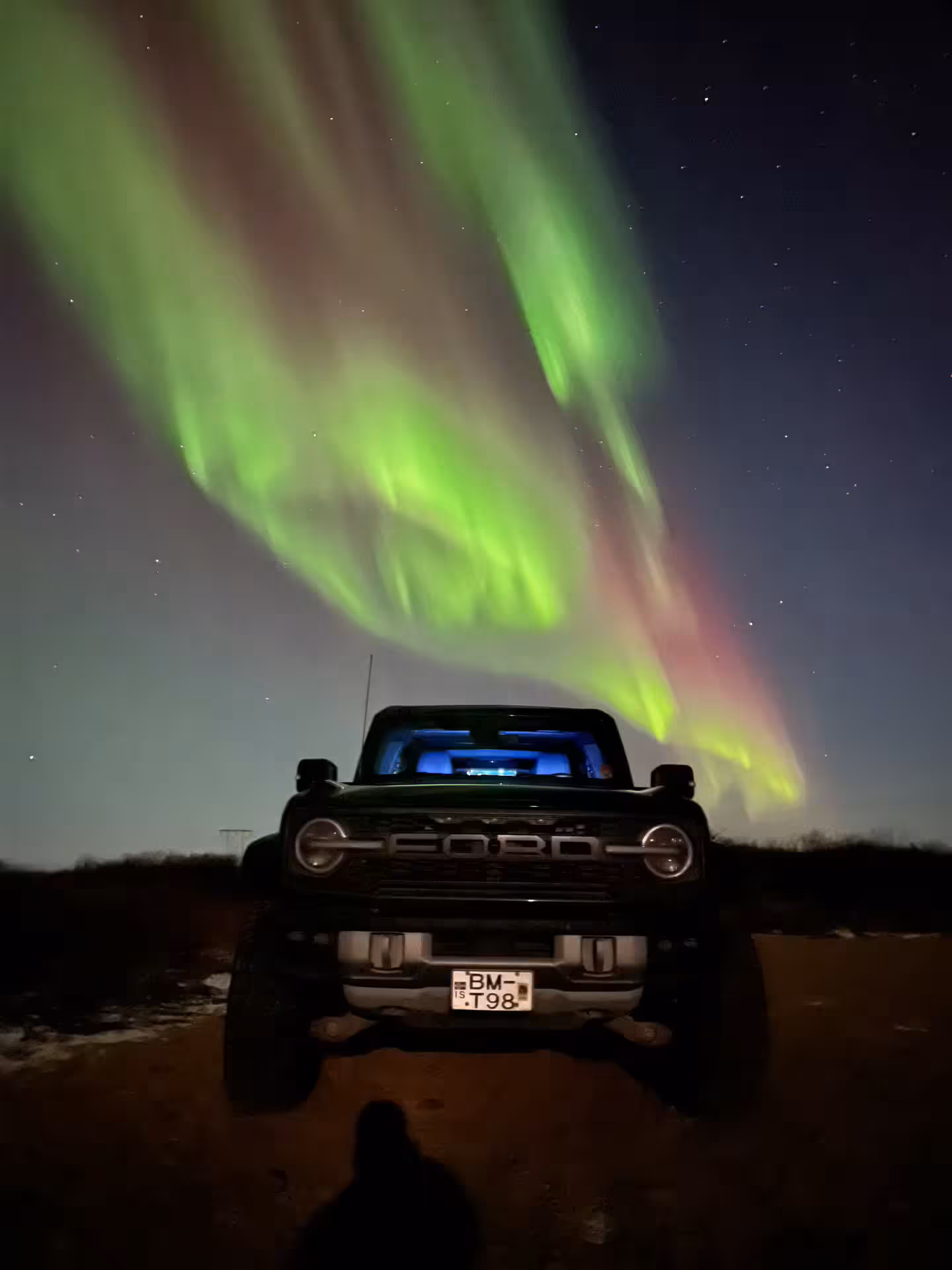 Ford Bronco 4x4 parked under vivid green and red aurora borealis in Iceland night sky