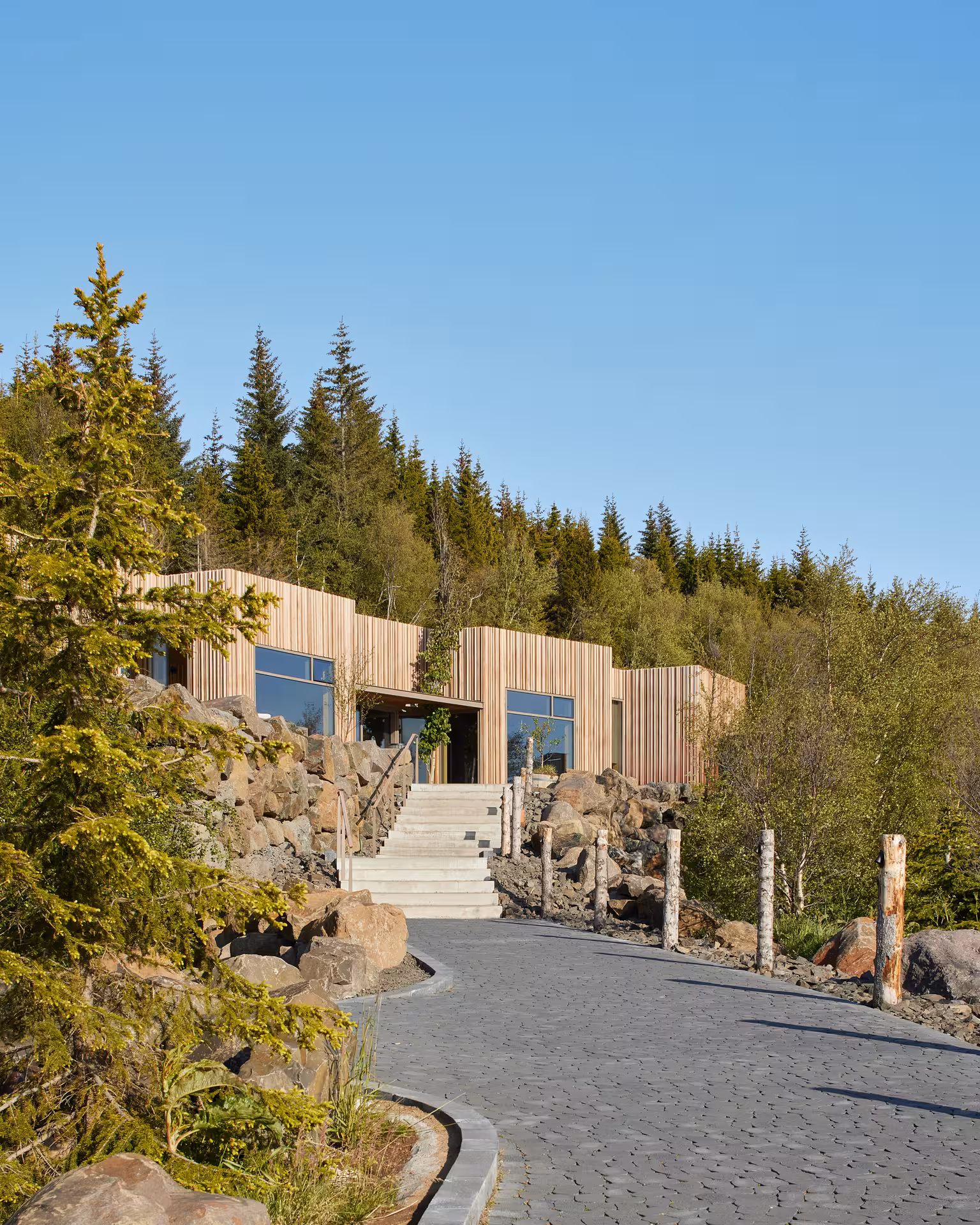 Forest Lagoon entrance with wooden clad building nestled among rocks and pine trees in Akureyri Iceland