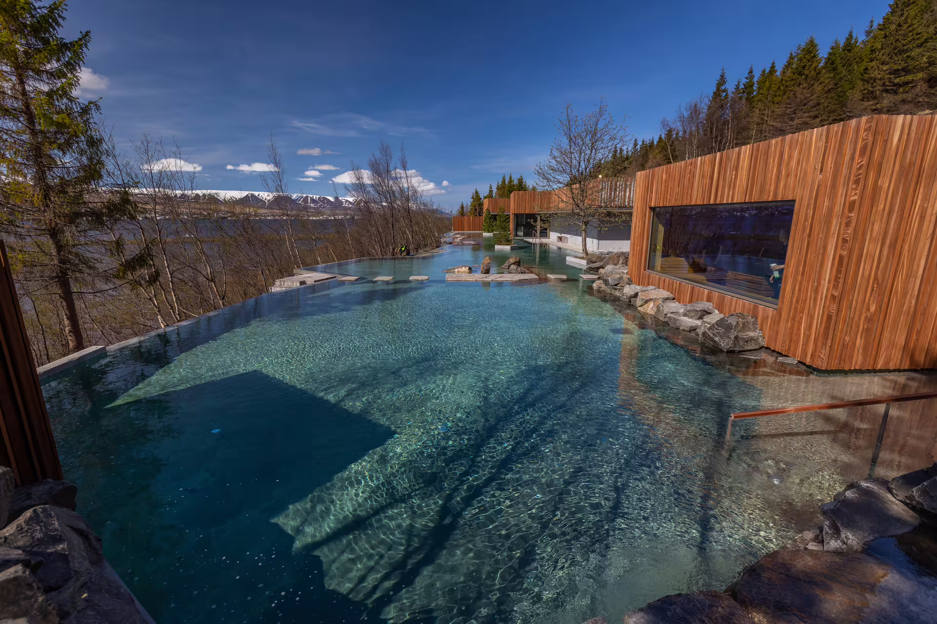 Forest Lagoon infinity pool with turquoise geothermal waters surrounded by trees and snow-capped mountains in Iceland