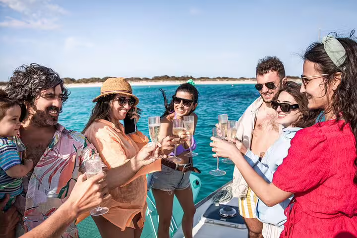 Group enjoying a catamaran tour near Formentera and Ibiza, toasting with drinks under sunny skies and turquoise waters.