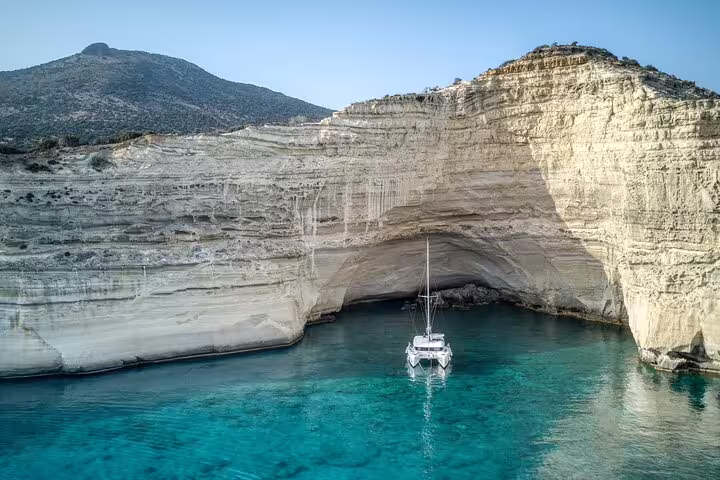 Catamaran anchored in a stunning turquoise cove beneath towering cliffs on the Formentera and Ibiza small group tour.