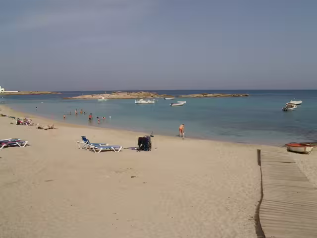 Calm Formentera lagoon beach with sunbeds and boats, ideal stop on Ibiza to Formentera fast ferry day trip