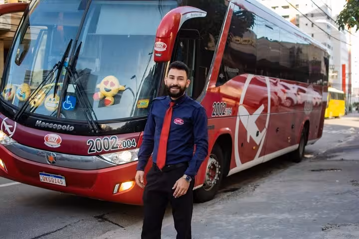 Driver welcoming guests beside red coach for Fortaleza to Jericoacoara transfer with luggage support