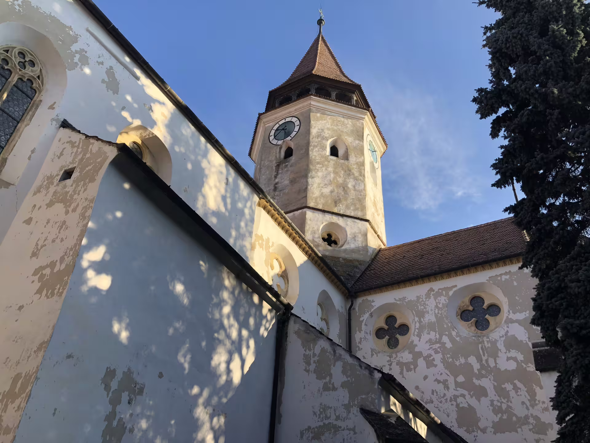 Gothic fortified church tower with clock face and peeling whitewashed walls in Brasov, Transylvania