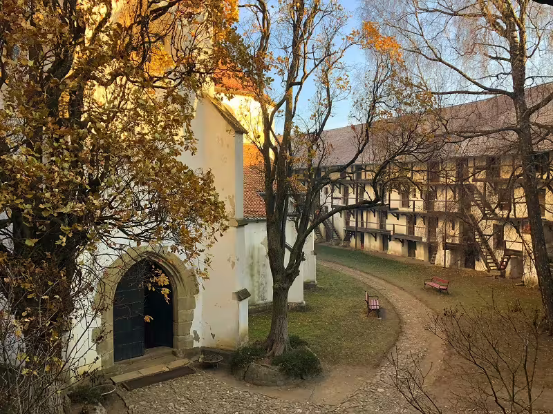 Medieval fortified church courtyard with half-timbered gallery building surrounded by autumn trees in Transylvania