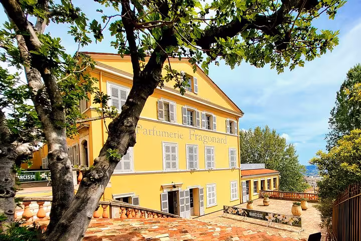 Charming yellow Parfumerie Fragonard building amidst lush greenery in Côte d'Azur hinterland tour.