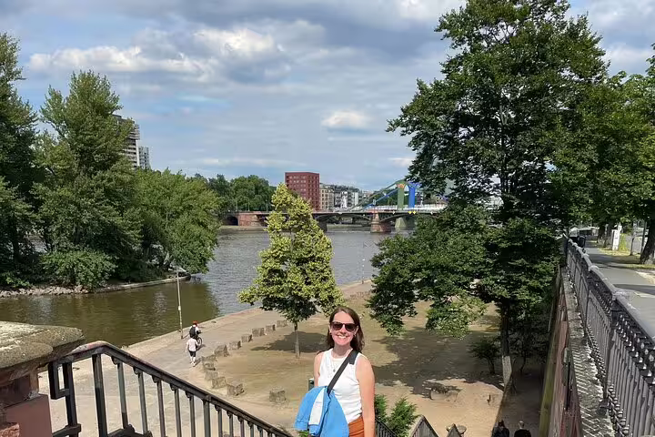 Smiling woman with blue backpack on steps overlooking the Main River and bridge in Frankfurt Old Town