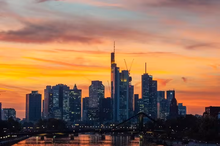 Frankfurt skyline at sunset with illuminated skyscrapers and river bridge in the foreground