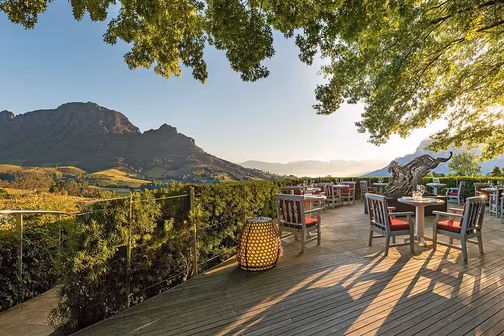 Scenic view of a sunlit terrace in Franschhoek with elegant seating and stunning mountain vistas in the Cape Winelands.
