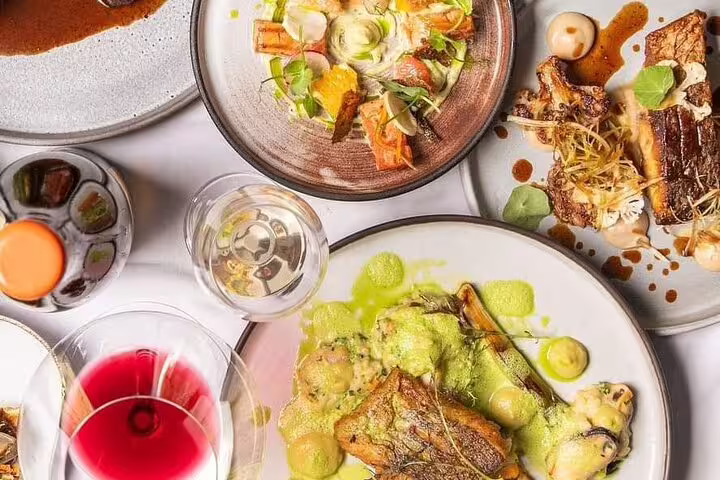 Assorted gourmet dishes with vibrant sauces and wine glasses on Franschhoek Tram Explorer Tour culinary journey.