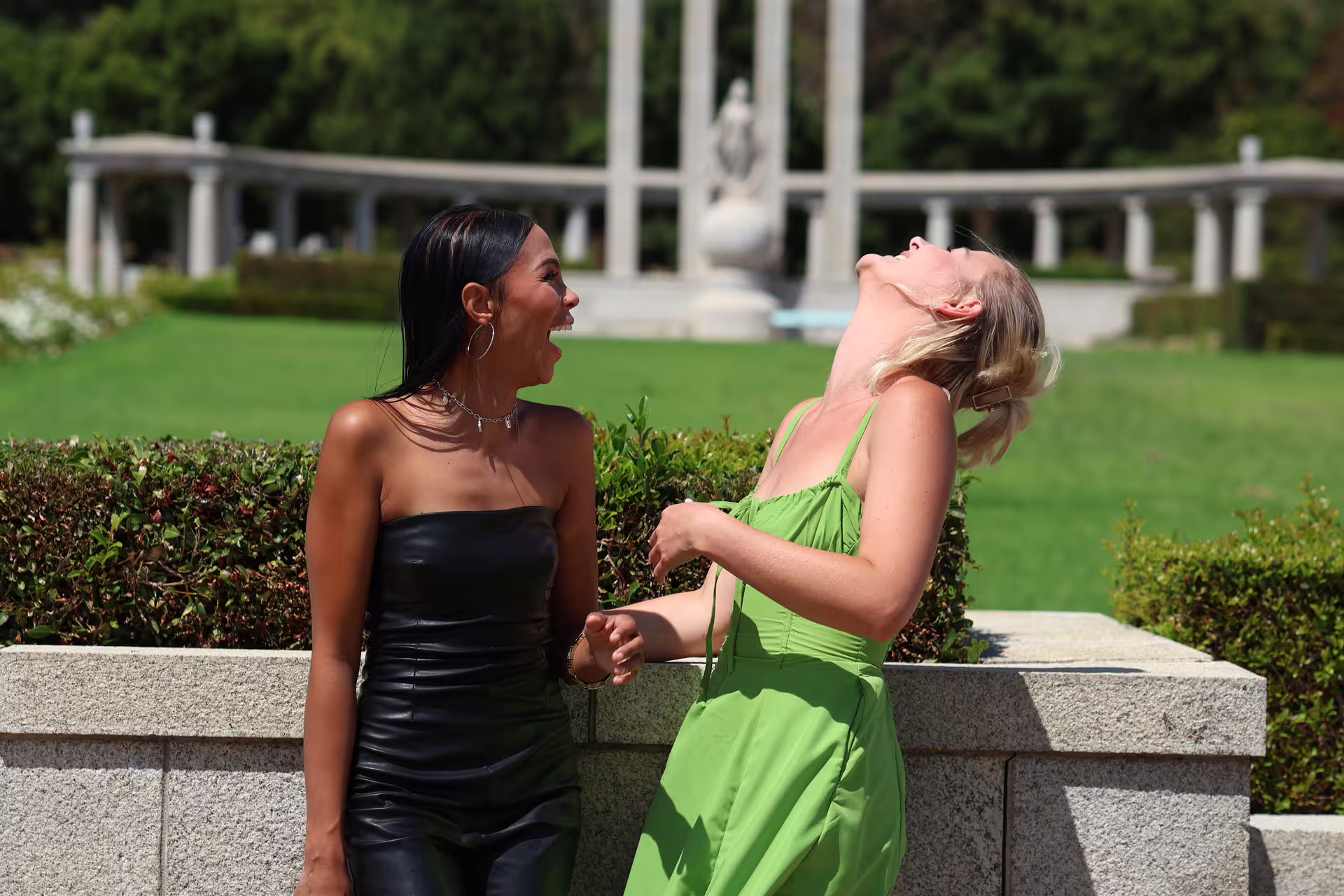Two friends laughing in a sunny garden setting, enjoying the Franschhoek wine tram experience.
