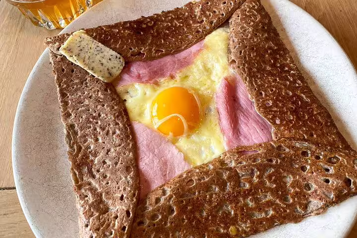 Traditional French buckwheat galette with egg, ham and cheese on a white plate