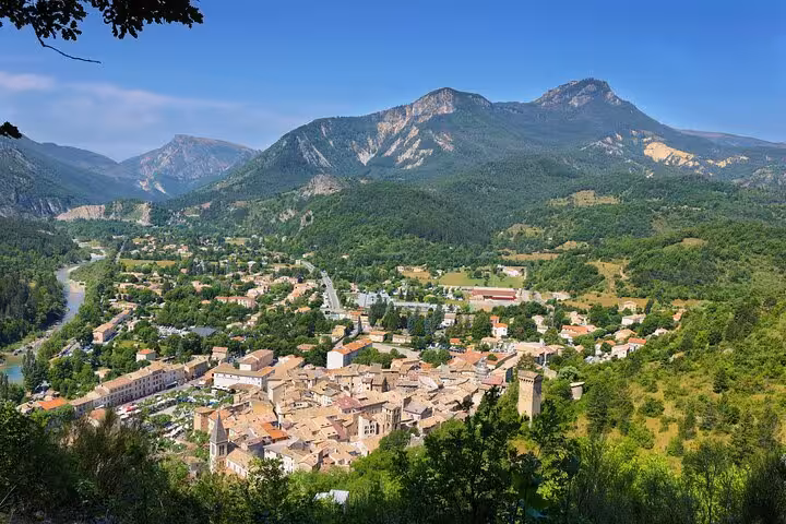Aerial view of a French alpine village with terracotta rooftops, river, and lush mountain backdrop