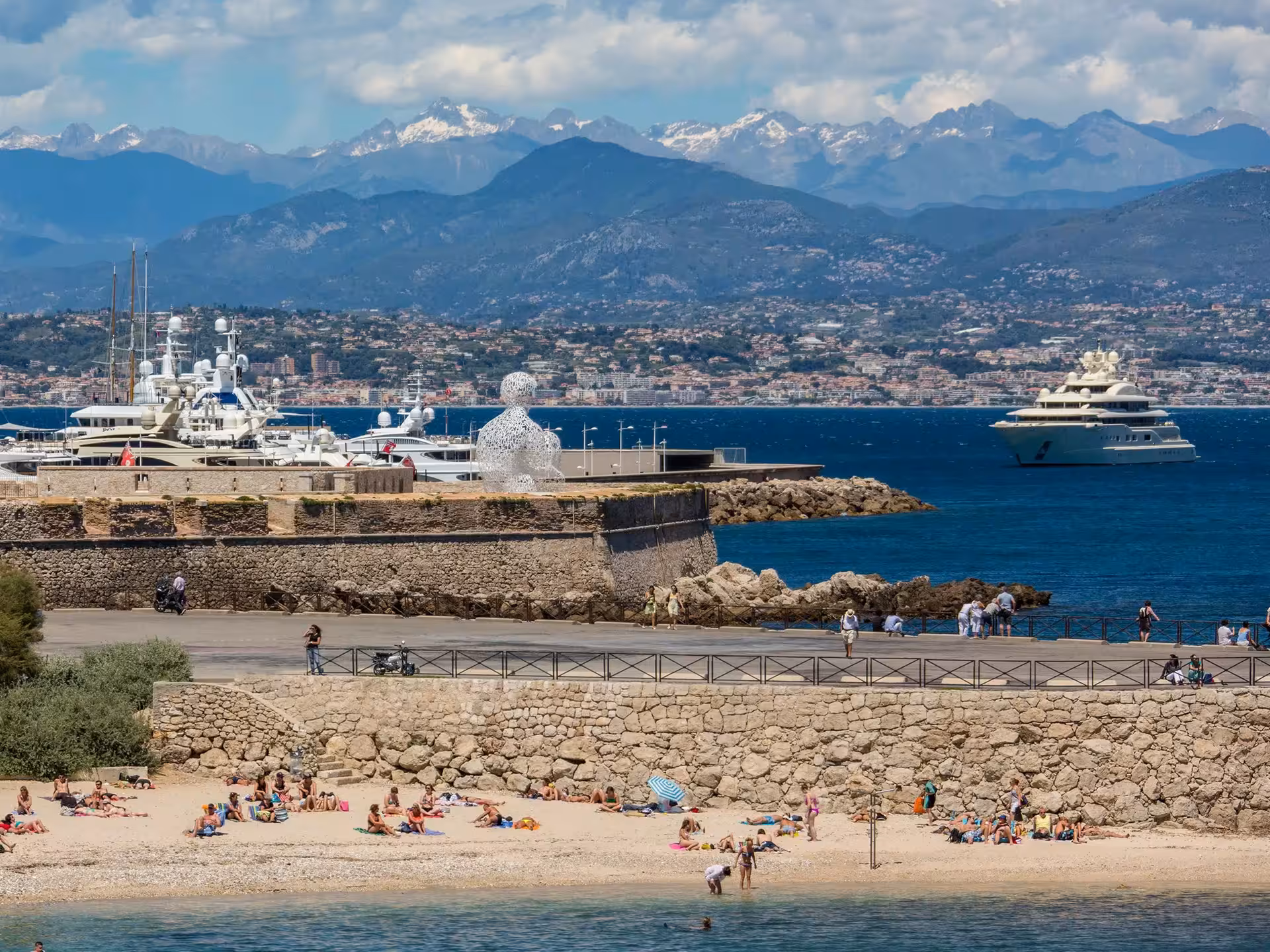 Antibes beach and marina with luxury yachts, French Riviera coastline, and snow-capped Alps in background