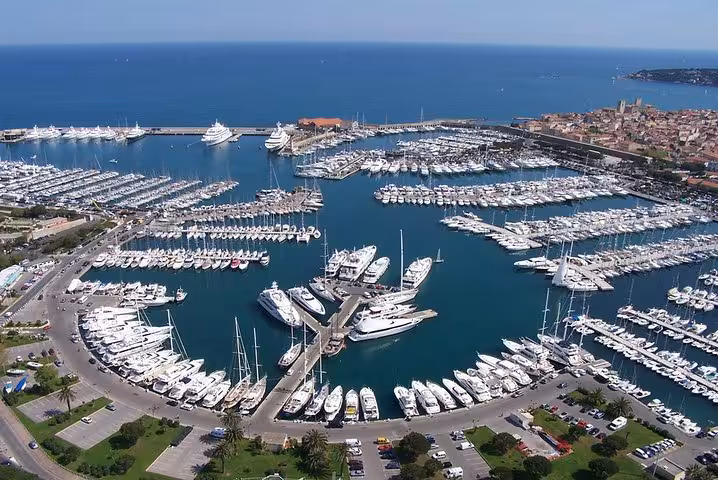 Aerial view of a bustling French Riviera marina packed with luxury yachts and sailboats near a coastal village