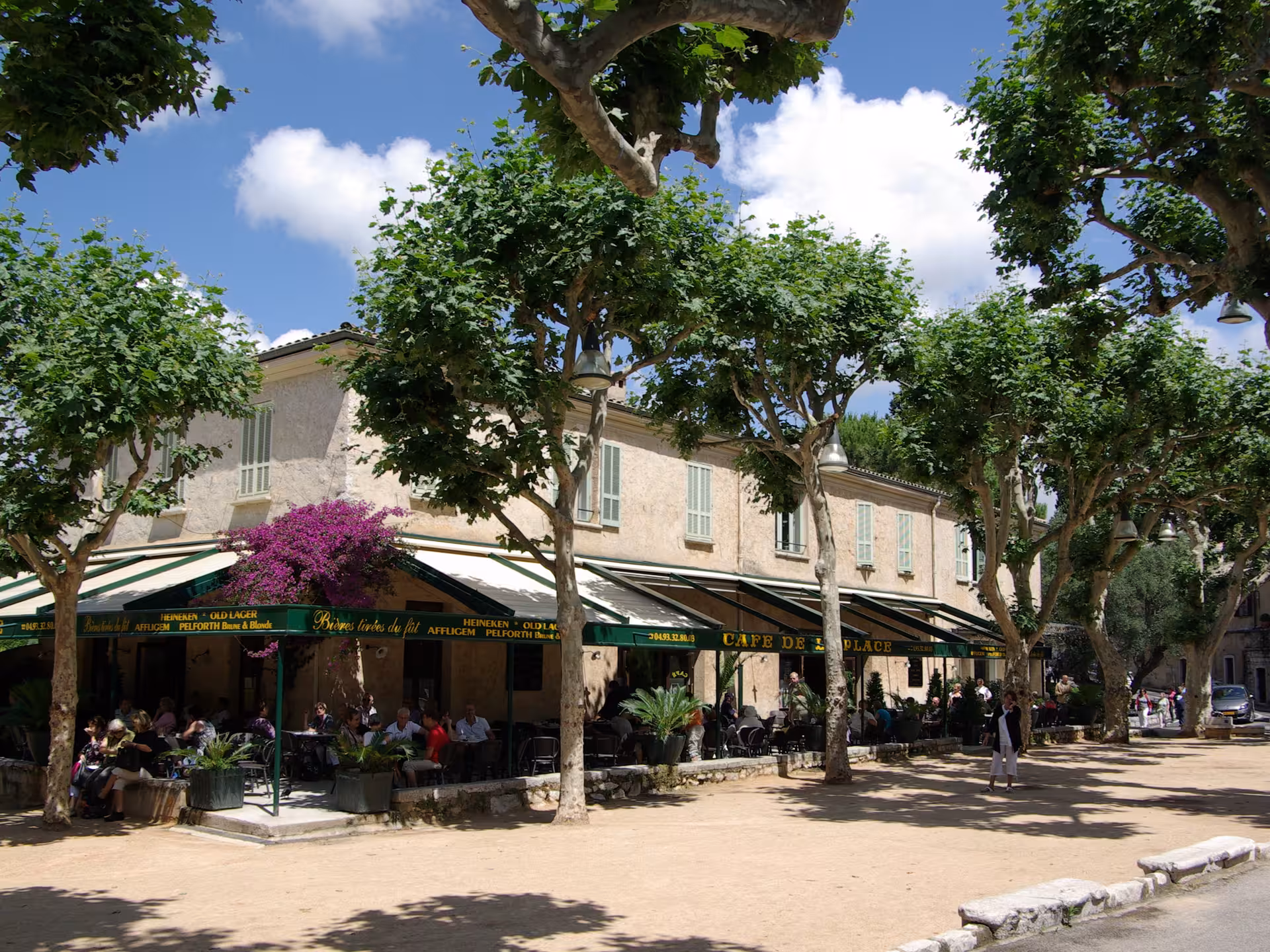 Sunny outdoor cafe terrace with green awnings and plane trees on a French Riviera village square