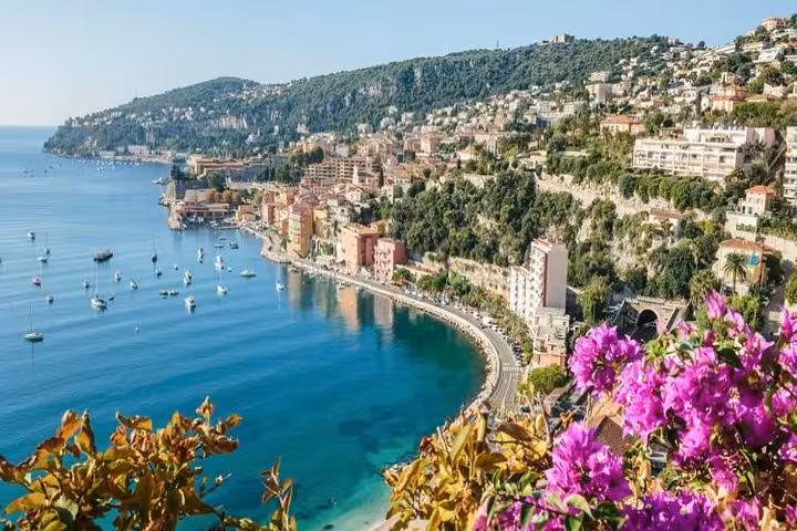 Aerial view of French Riviera coastline with turquoise sea, colorful buildings, and pink bougainvillea flowers