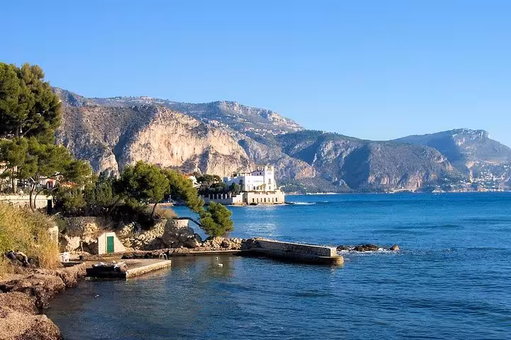 Rocky coastline with blue sea, pine trees, white villa, and dramatic cliffs on the French Riviera near Nice