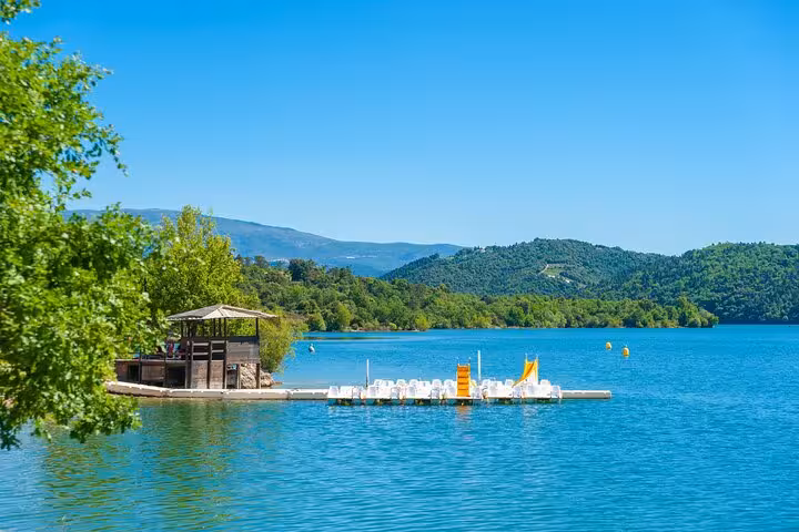 Turquoise lake with floating dock and water activities surrounded by green hills in French Riviera countryside