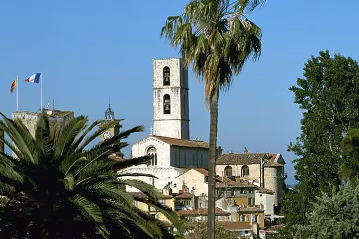 Medieval church tower and village rooftops with palm trees and French flag on French Riviera countryside