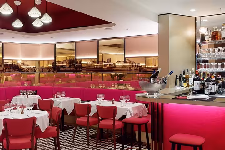 Elegant pink restaurant interior with set dining tables and bar area for French Riviera dinner