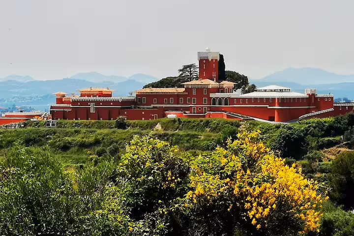 Red hilltop castle surrounded by lush greenery and yellow wildflowers in the French Riviera countryside