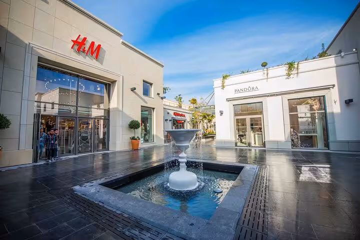 Chic shopping area in French Riviera with H&M and Pandora stores, featuring a central fountain under a clear blue sky.
