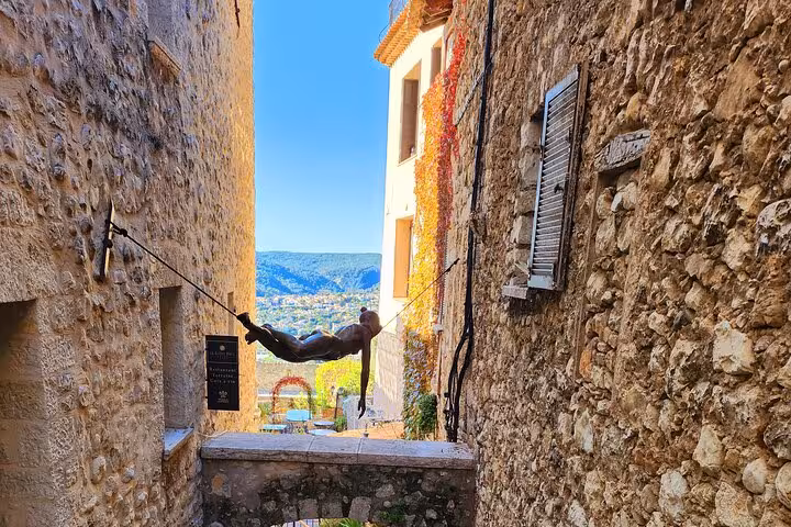 Narrow stone alley with artistic sculpture and stunning French Riviera view.