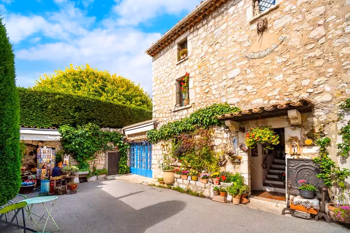 Charming stone building with ivy, colorful potted flowers, and blue doors in a village courtyard, French Riviera