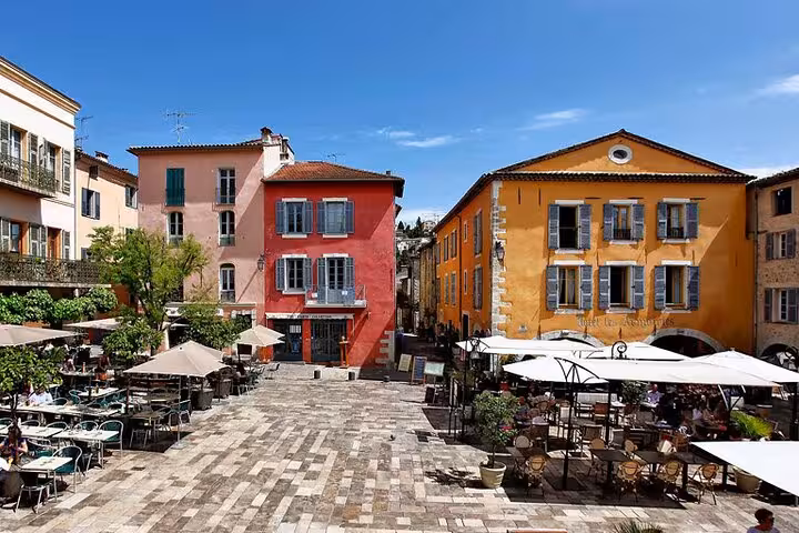 Colorful buildings and outdoor café terraces on a sunny cobblestone square in the French Riviera countryside