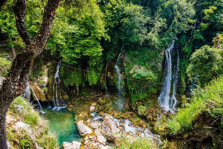 Multiple cascading waterfalls flowing into turquoise pool surrounded by lush green forest