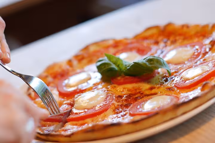 Close-up of a freshly baked Margherita pizza being enjoyed, showcasing a delicious outcome from a Naples cooking class.