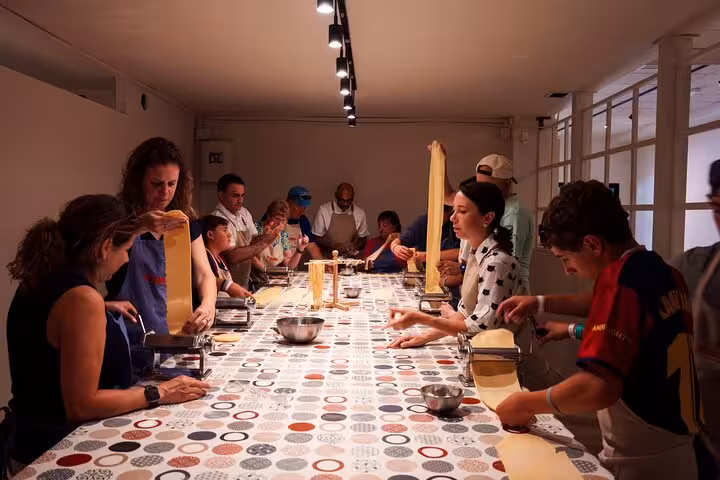 Group of people making fresh pasta in a bright kitchen during a cooking class in Barcelona.