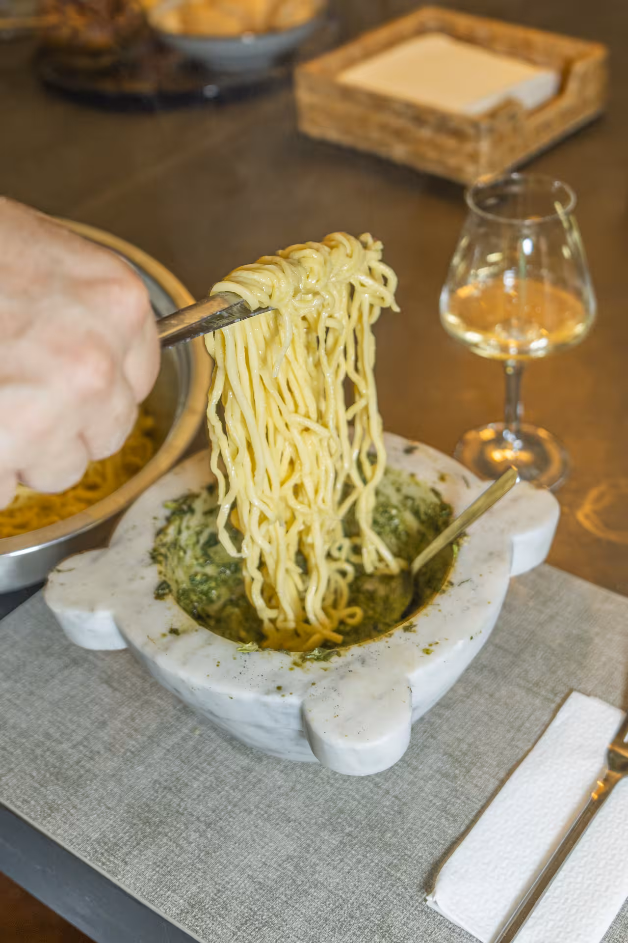 Fresh pasta being mixed with homemade pesto in a marble bowl, accompanied by wine, showcasing Italian cuisine in Liguria.