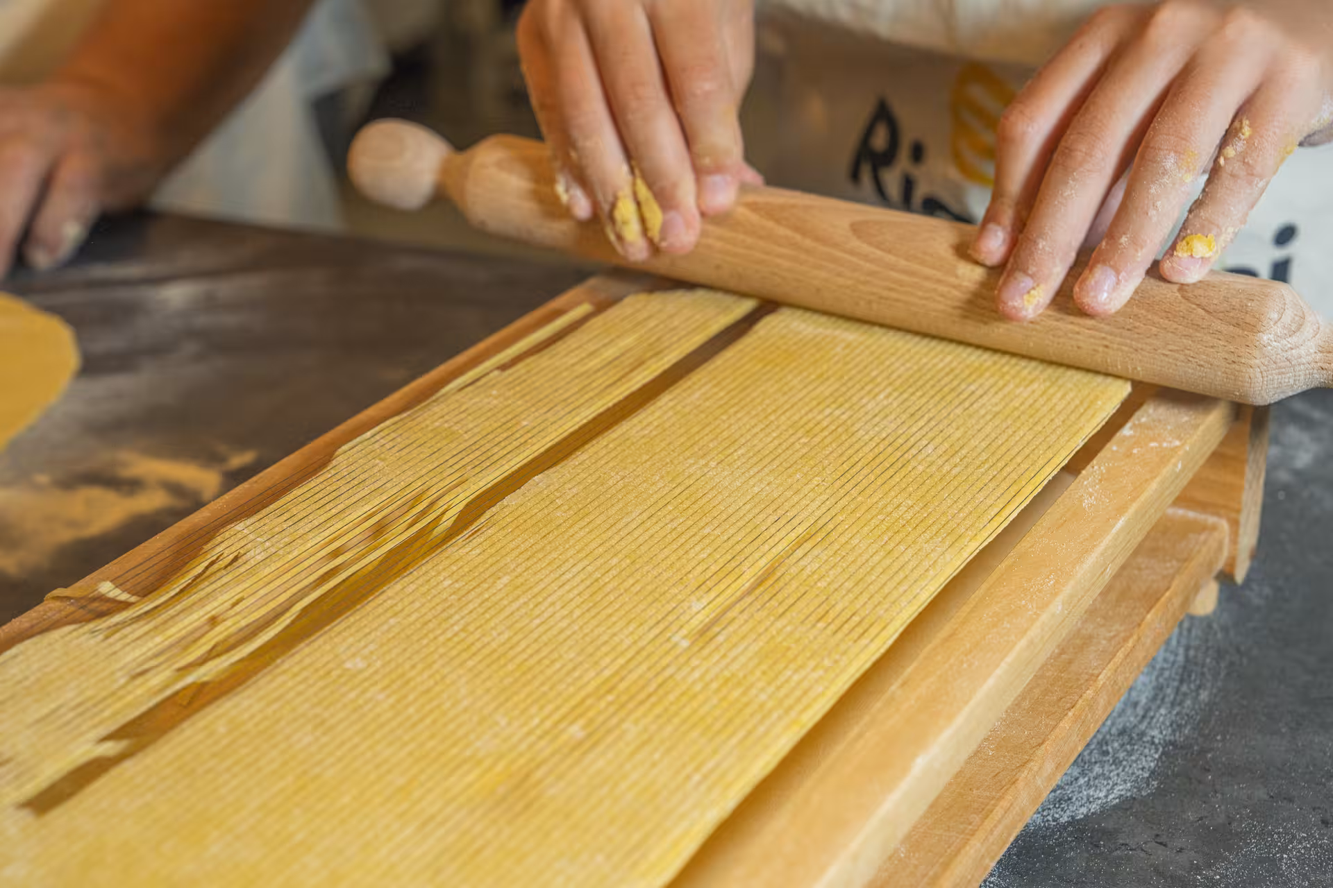 Hands skillfully rolling fresh pasta dough on a wooden board during a culinary class in the Portofino-Cinque Terre tour.