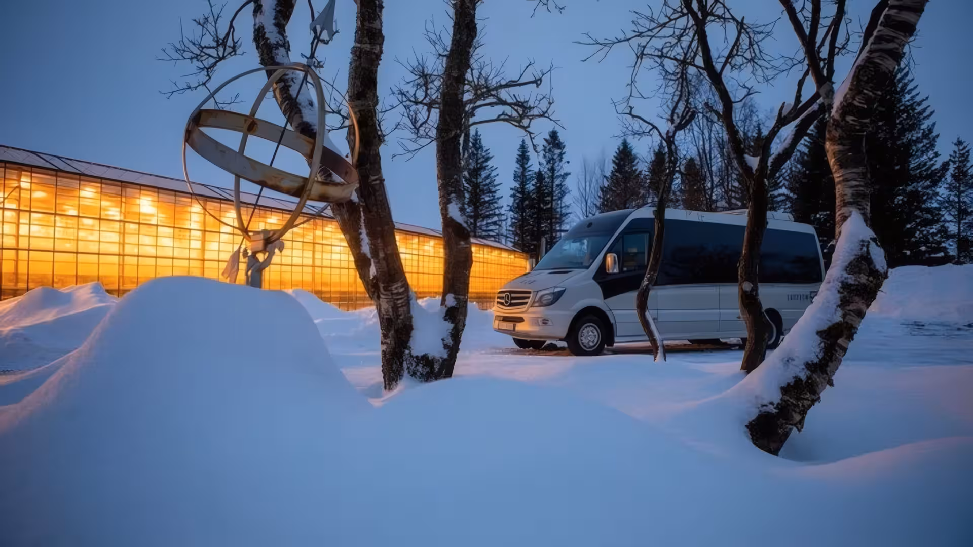 White Mercedes minibus parked outside Fridheimar Farm glowing greenhouse in snowy Iceland winter dusk