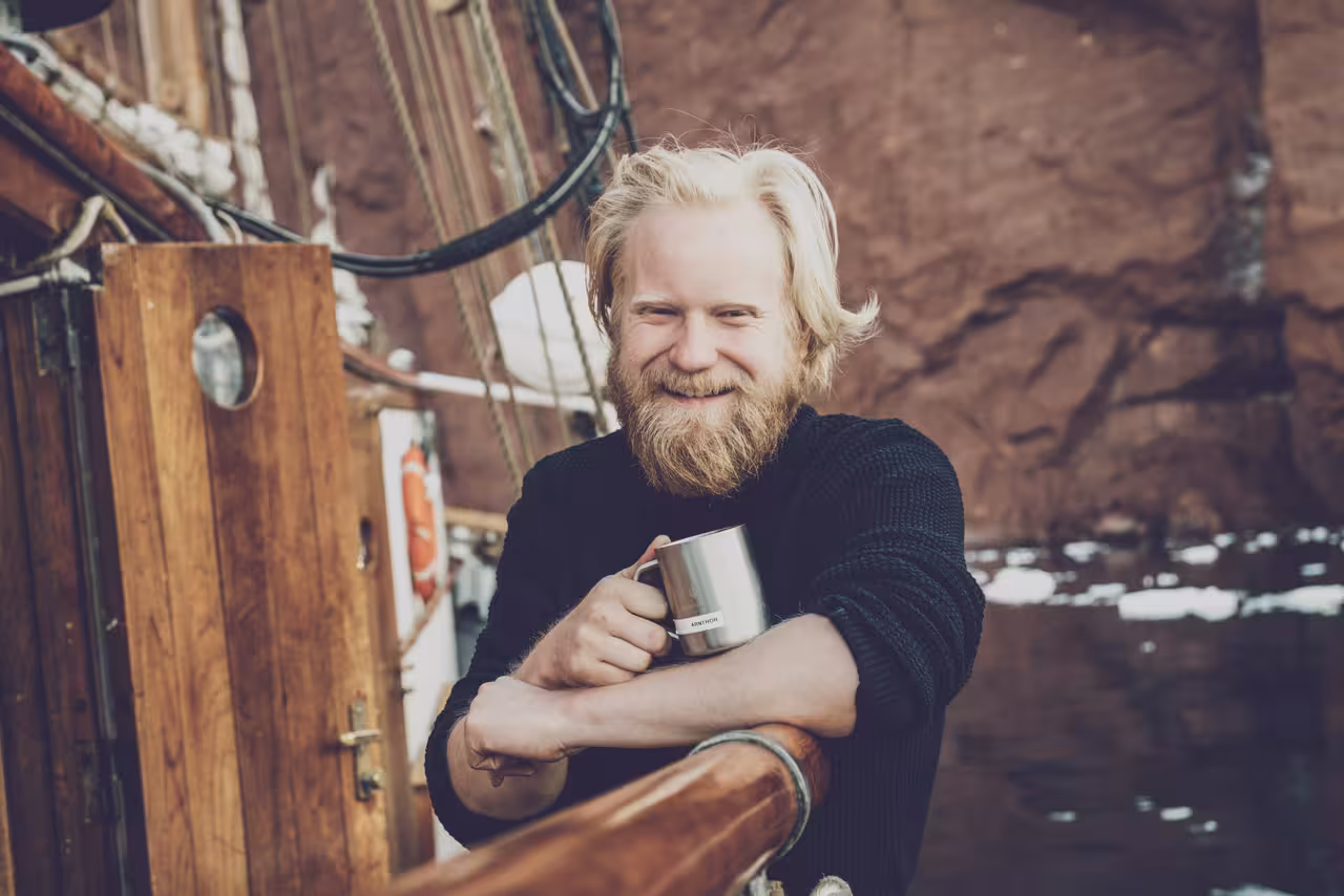 Friendly crew member smiling with a warm mug aboard an exclusive Northern Lights luxury cruise ship