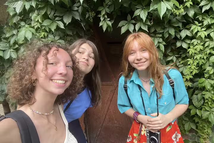 Three young women smiling in front of ivy-covered wooden door in Budapest