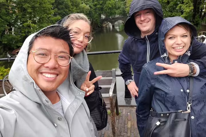 Friends in rain by a scenic canal, enjoying a self-guided Pisa e-scavenger hunt city exploration game