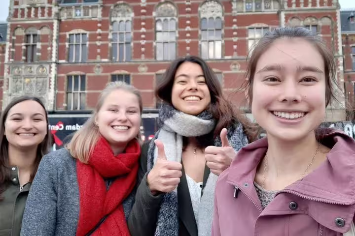 Friends smiling on Dam Square during an Amsterdam e-scavenger hunt, self-guided smartphone walking tour
