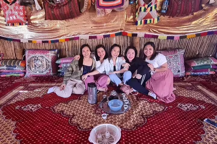 Group of friends relax in traditional desert tent, sharing tea and laughter during private full-day desert tour.