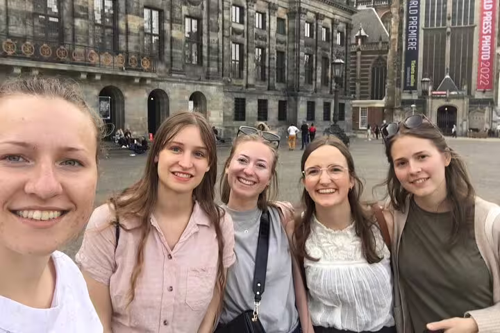 Five smiling women posing for selfie at Amsterdam Dam Square historic building
