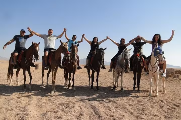 Friends on horseback in Hurghada desert raising hands, fun 2-hour beach and desert riding tour