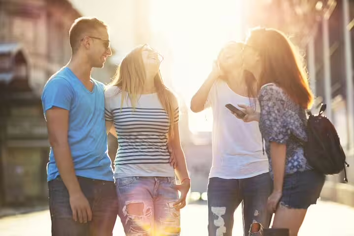 Friends in sunlight checking phones on a Leuven e-scavenger hunt, enjoying a self-guided walking adventure