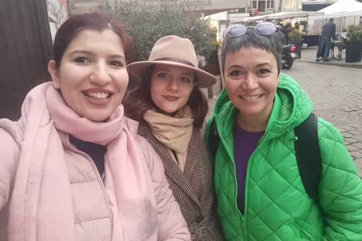 Three smiling women posing together in historic Ghent city center during outdoor escape game tour
