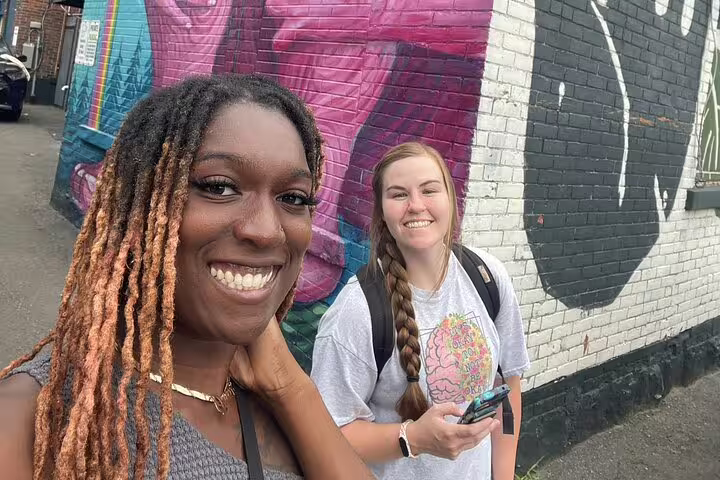 Two smiling women posing in front of colorful street art murals in Ottawa
